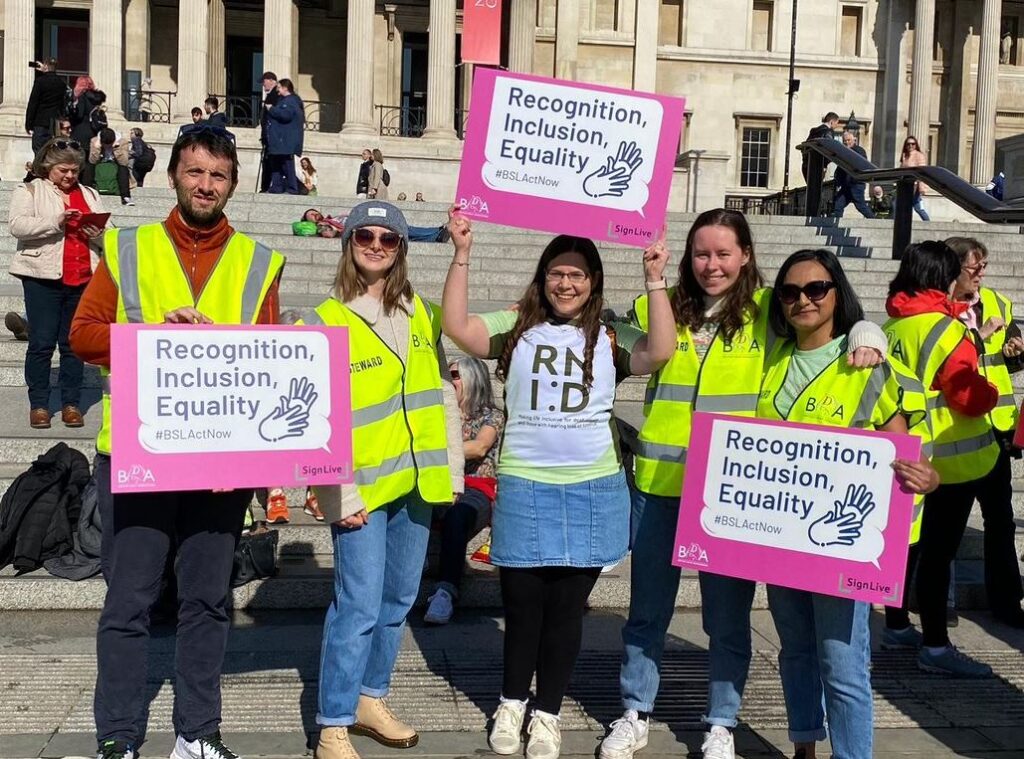 RNID campaigners pose with posters which read 'recognition, inclusion, equality'