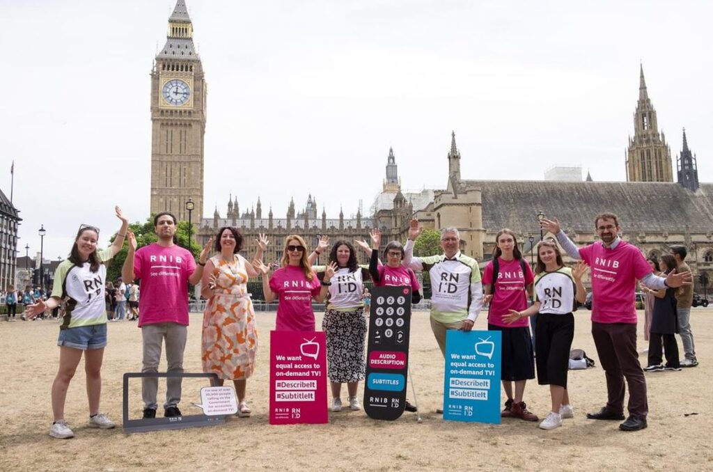 A photo of RNID and RNIB campaigners, standing outside of the Houses of Parliament with placards and waving their hands at the camera. 