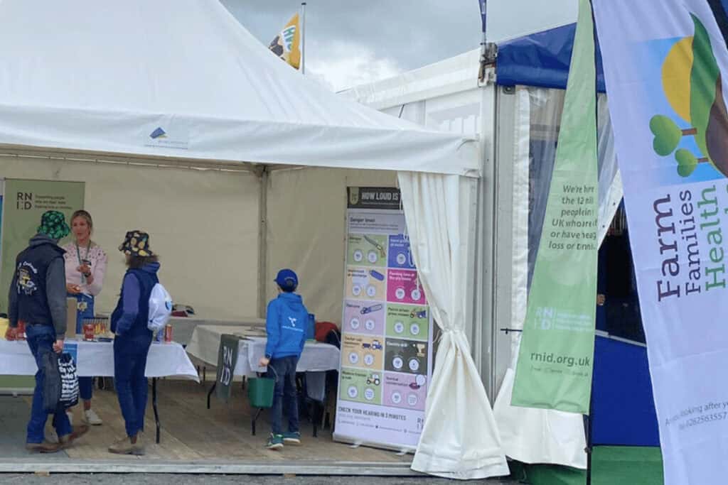 A RNID volunteer speaking with visitors at the Balmoral Show, in an outdoor tent.