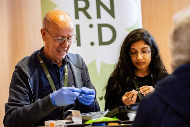 Two people at an RNID event stand, seated and handling hearing devices.