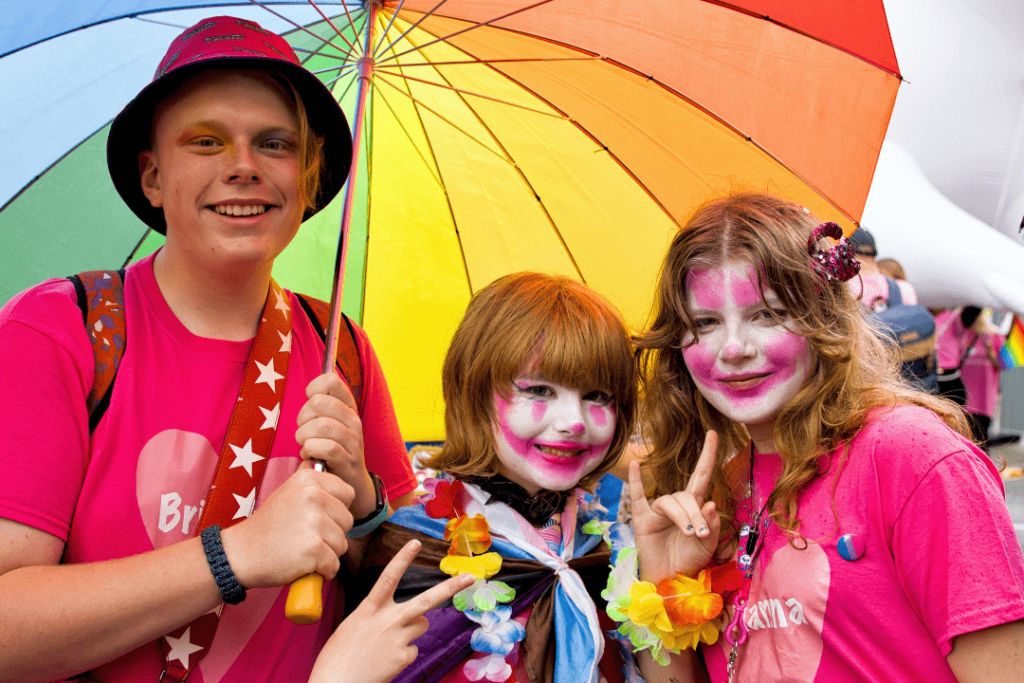 Three people in bright coloured clothing, wearing face paint and smiling at the camera. 