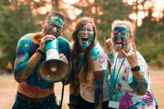 Three people are covered in paint. One of them holds a megaphone. They are all smiling.