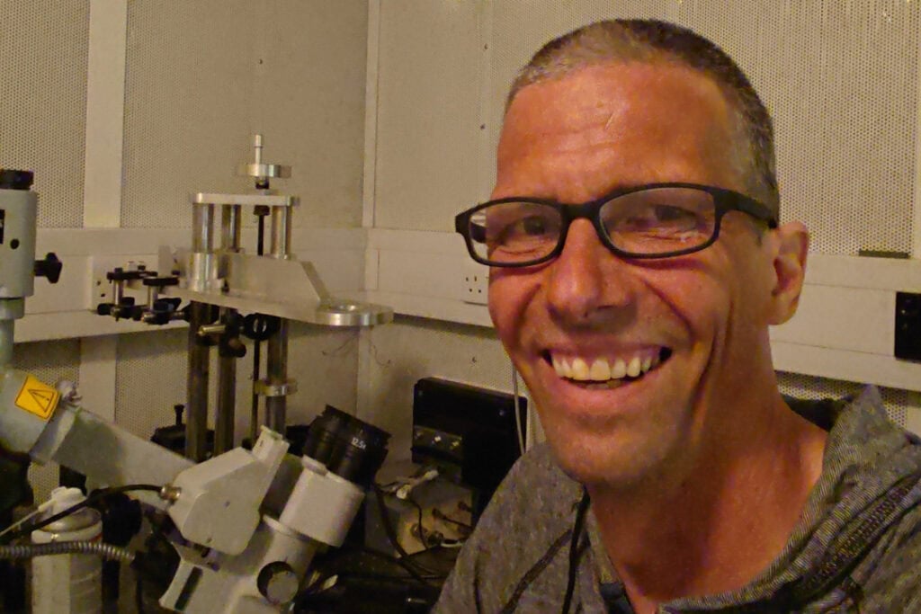 Rsearcher Dr Torsten Marquardt is in a laboratory. He wears glasses and smiles.