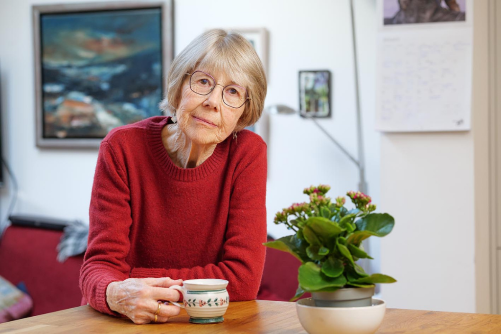Helen Kendall in her kitchen, wearing a red jumper and holding a cup of tea, looking at the camera