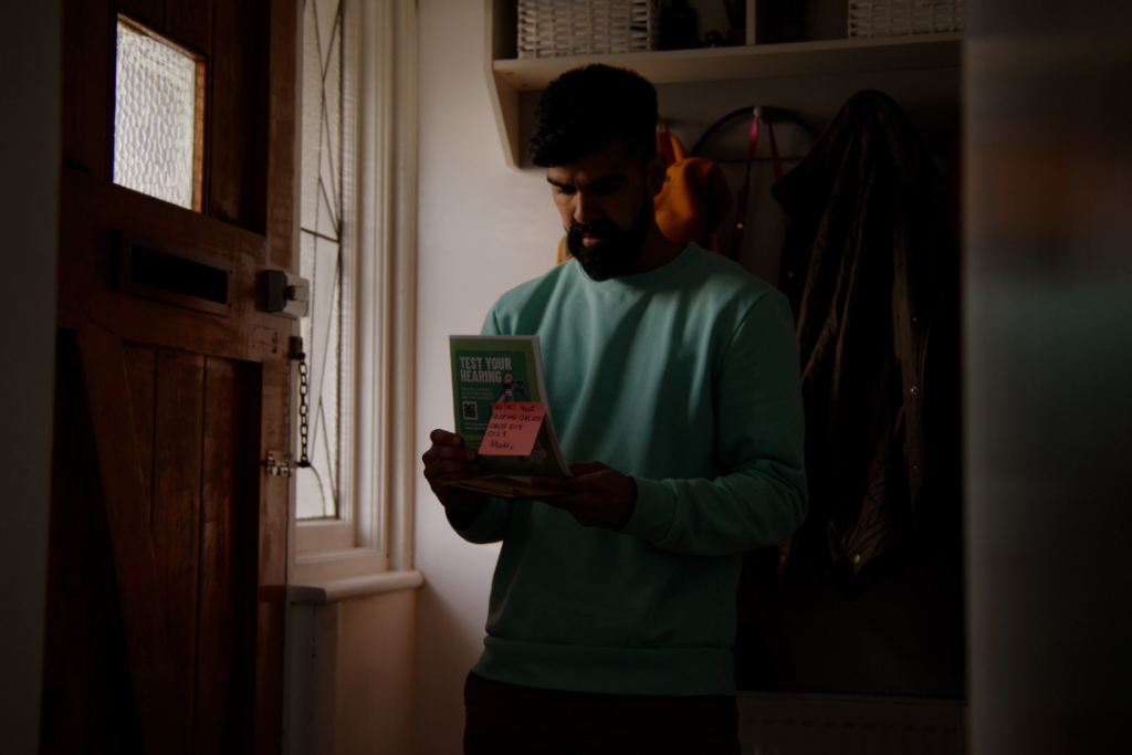 Shakib stands in his hallway, looking at the hearing aid leaflet his mother left out for him