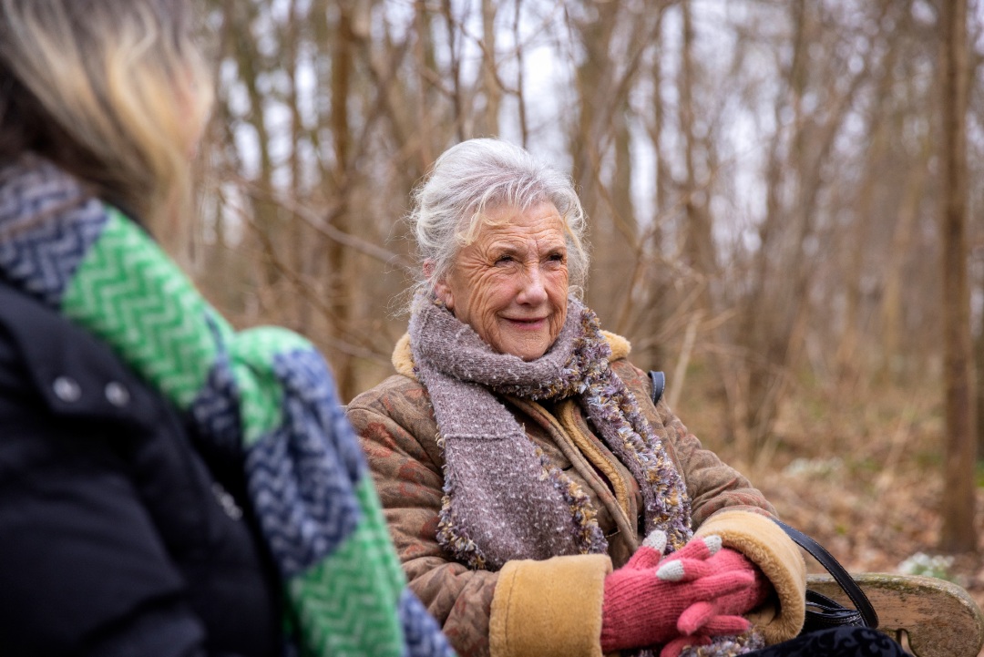 Two women wrapped up warm from the cold, sitting in a woodland area