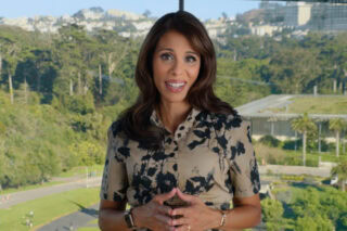 Dr Sumbul Desai from Apple. She stands in front of a large window showing a park and houses in the background, and she smiles at the camera.