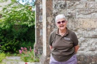 An RNID volunteer stands outside in a garden and smiles at the camera.