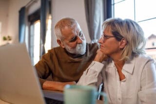 A man and a woman looking at each other in front of a laptop at home