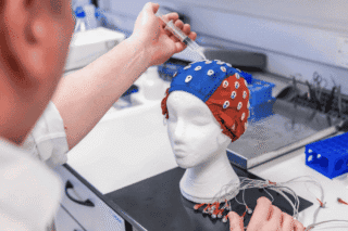 Photo of tinnitus researchers at Newcastle University in a lab, holding a syringe above a cap on a polystyrene head as part of an experimental setup.